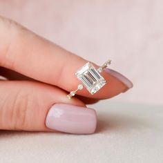 a woman's hand holding an engagement ring with a diamond in the middle and two diamonds on each side