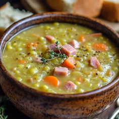 a bowl of soup with ham and carrots in it on a table next to bread