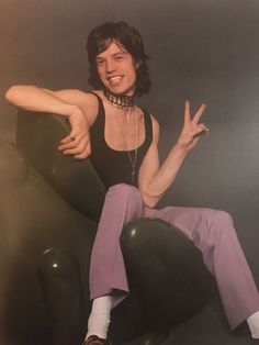 a woman sitting on top of a black chair with her arms out and hands in the air