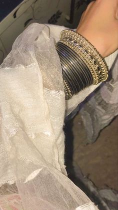 a woman's arm with several bracelets on top of it and an object in the background