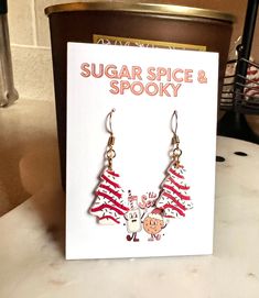 a pair of red and white christmas tree earrings sitting on top of a counter next to a card