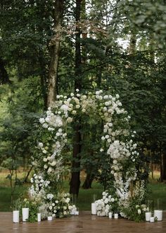 an outdoor ceremony setup with white flowers and candles on the ground in front of trees