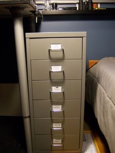 a filing cabinet sitting next to a bed in a bedroom