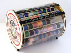 an assortment of different colored spools of thread in a metal container on a white surface