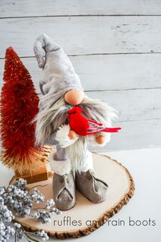 a stuffed bird sitting on top of a piece of wood next to a christmas tree