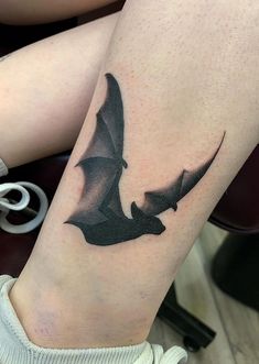 a woman's leg with a black and grey bat tattoo on her left thigh