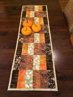 two orange pumpkins sitting on top of a table next to a quilted runner