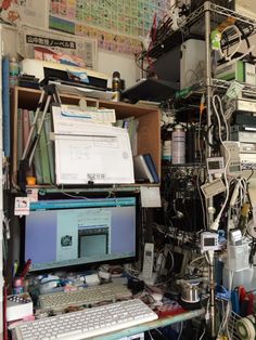 a cluttered desk with a computer monitor and keyboard on it, surrounded by wires