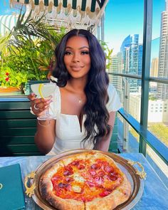 a woman sitting at a table with a pizza in front of her and a glass of wine