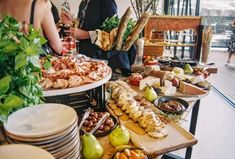 people are standing around a buffet table full of food and drinks, including breads