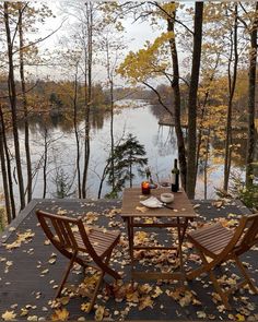 an outdoor table and chairs on a deck with autumn leaves around it, overlooking a lake