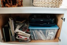 an open cabinet filled with books and other items next to a basket on top of it