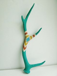 a small green sculpture with a colorful design on it's head and arms in the shape of a tree branch