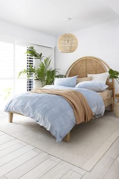 a bed with blue sheets and pillows in a bedroom next to a plant on the floor