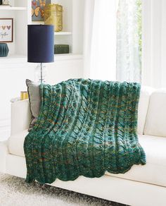 a couch with a green blanket on top of it next to a lamp and window