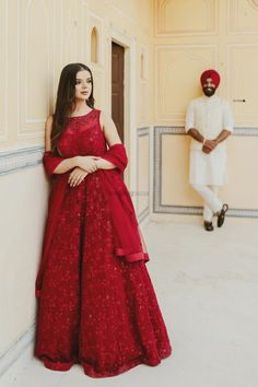 a woman in a red dress leaning against a wall next to a man in a white turban