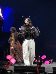 a woman standing on top of a stage next to another person wearing white pants and black jacket