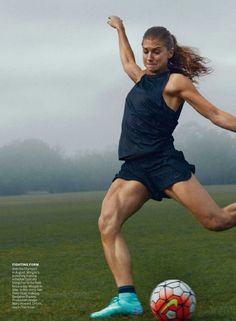 a woman kicking a soccer ball on top of a field