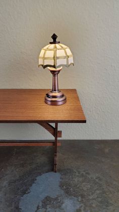 a table lamp sitting on top of a wooden table in front of a white wall