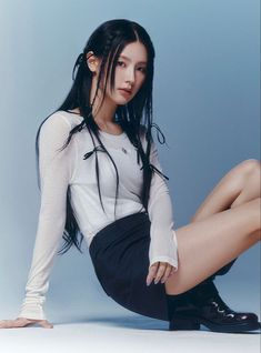 a woman with long black hair and white shirt sitting on the ground wearing high heels