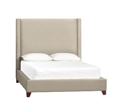 an upholstered bed with white sheets and pillows