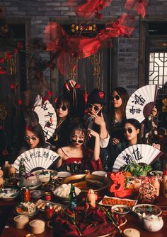 a group of women dressed up in costumes and holding fans pose for a photo with food on the table