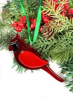 a red bird ornament sitting on top of a green christmas tree next to berries and pine cones