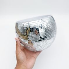 a hand holding up a silver disco ball in front of a white background with the reflection of a dog on it