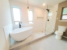 a large white bathtub sitting next to a toilet in a bathroom under two windows