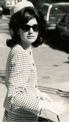 an old photo of a woman on the sidewalk with her hand in her pocket and wearing sunglasses