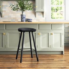 a black stool sits in front of a kitchen counter with green cabinets and white walls