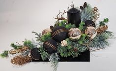 a black candle surrounded by greenery and pine cones with silver balls in the center