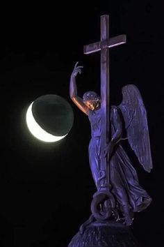 a statue of an angel holding a cross on top of a hill with the moon in the background