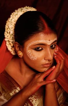 a woman with white face paint on her face and red scarf around her neck, holding her hands to her face