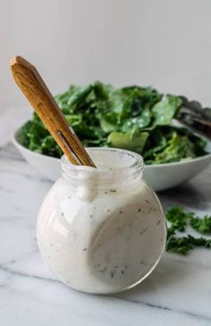 a salad in a jar with a wooden spoon next to it on a marble table