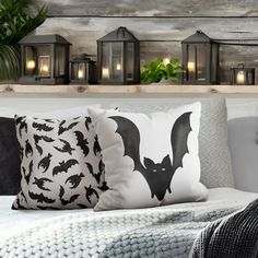 a bed topped with lots of pillows covered in black and white bat pillow cases next to candles