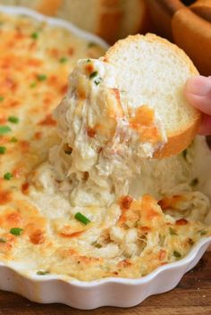 a hand holding a piece of bread over a casserole dish