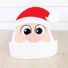 a paper santa claus hat with eyes and nose on a wooden floor next to a white wall