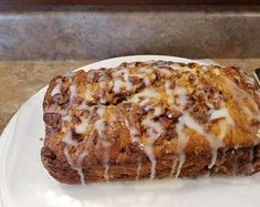 a white plate topped with a loaf of bread covered in icing next to a fork