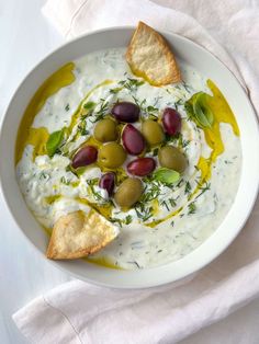 a white bowl filled with olives, cheese and crackers on top of a table