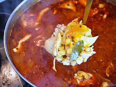 a pot filled with soup and vegetables being stirred by a ladle to stir it