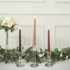 three candles are sitting on a table with flowers and greenery