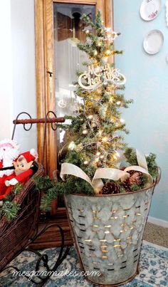 a small christmas tree in a metal basket on the floor next to a mirror and other decorations