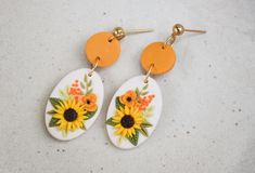 the earrings are decorated with sunflowers and orange flowers on white oval shaped ear wires