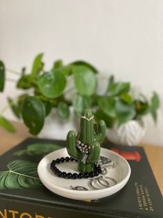 a green plant sitting on top of a book next to a white plate with black beads