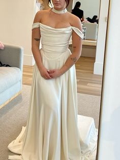 a woman standing in front of a mirror wearing a white dress with an off the shoulder neckline