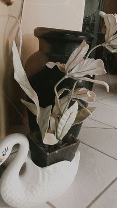 a white swan statue sitting on top of a tiled floor next to a potted plant