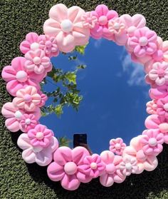 a mirror with pink flowers in the shape of a heart on top of green grass