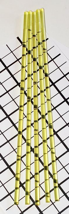 four yellow bamboo sticks sitting on top of a white table next to a black grid