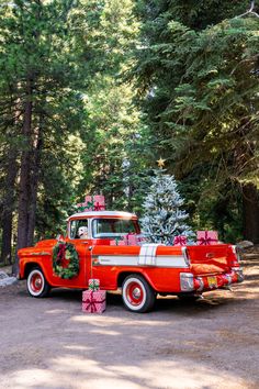 an old red truck with christmas presents on the back parked in front of some trees